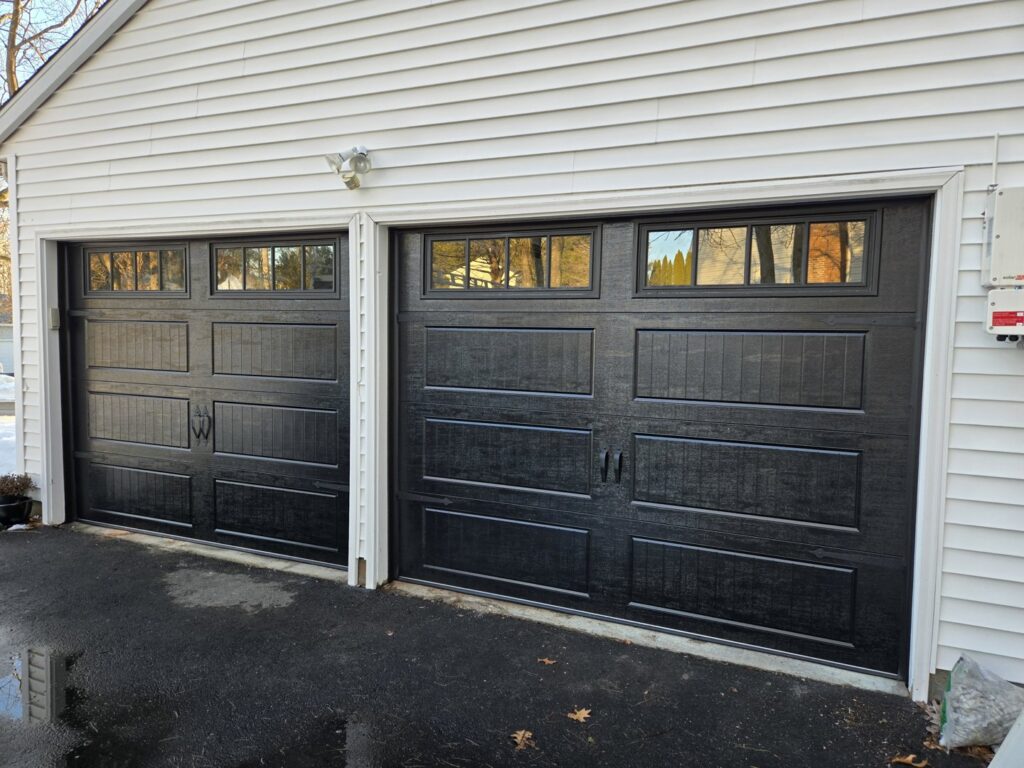 Two newly installed black garage doors with windows on a light-colored house by Spring King Garage Doors in Middletown, CT