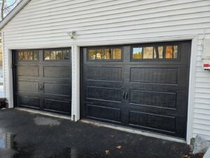 Two newly installed black garage doors with windows on a light-colored house by Spring King Garage Doors in Middletown, CT