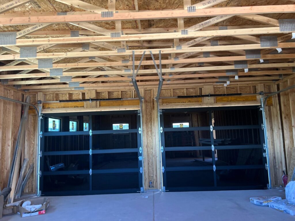 Two black modern garage doors with windows installed in a newly framed building by Excellence Garage DOORS LLC in Los Angeles, CA