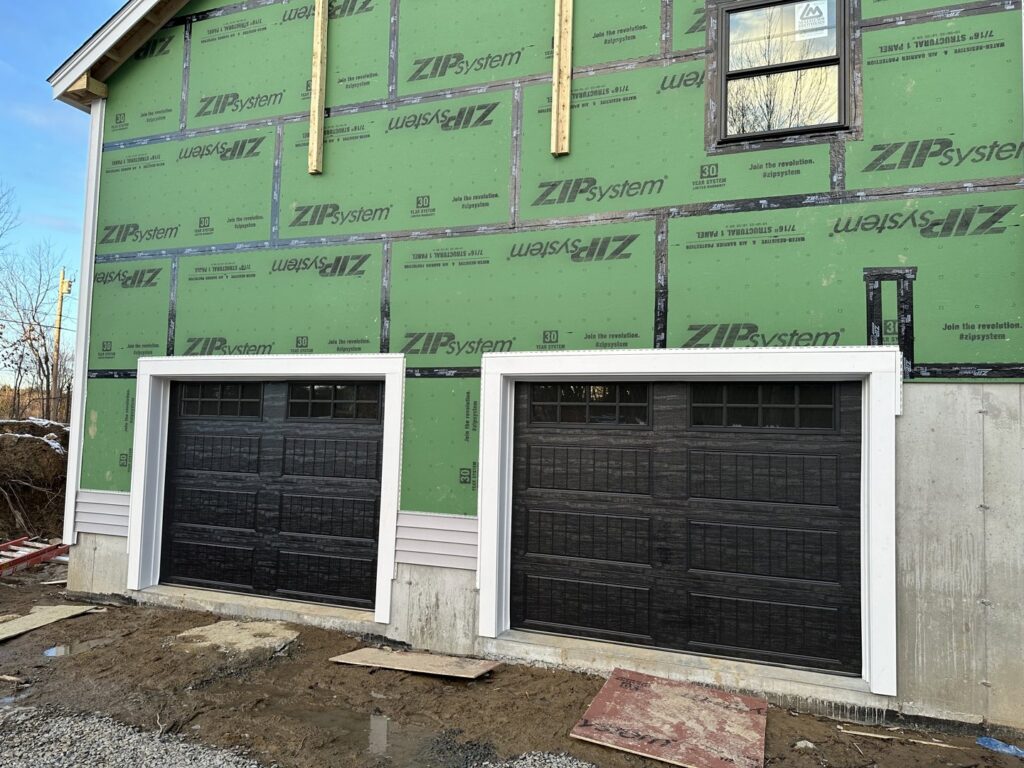 Two black panel garage doors installed on a new construction home with ZIP System sheathing by Steve Shumsky Unlimited Overhead Doors LLC in Hudson, NH