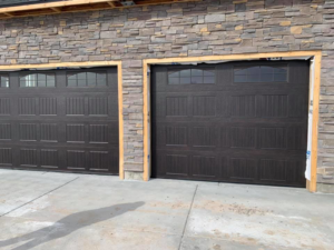 Two brown garage doors with windows installed in a new construction home by Next Level Garage Doors in Locust Grove, GA.