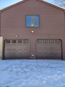 Two newly installed brown garage doors with windows on a brown-sided house by Spring King Garage Doors in Middletown, CT