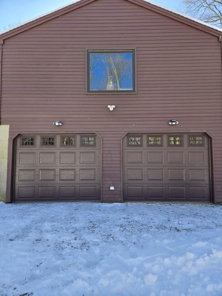 Two newly installed brown garage doors with windows on a brown-sided house by Spring King Garage Doors in Middletown, CT