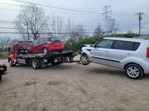 Two cars being towed, one on a flatbed and one with a wheel lift, by Vatos Locos Towing in Cincinnati, OH.