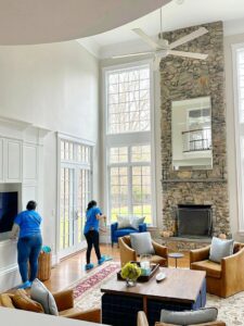 Two professional cleaners from Supreme Home Cleaning, Inc cleaning a spacious living room with high windows in Boston, MA.