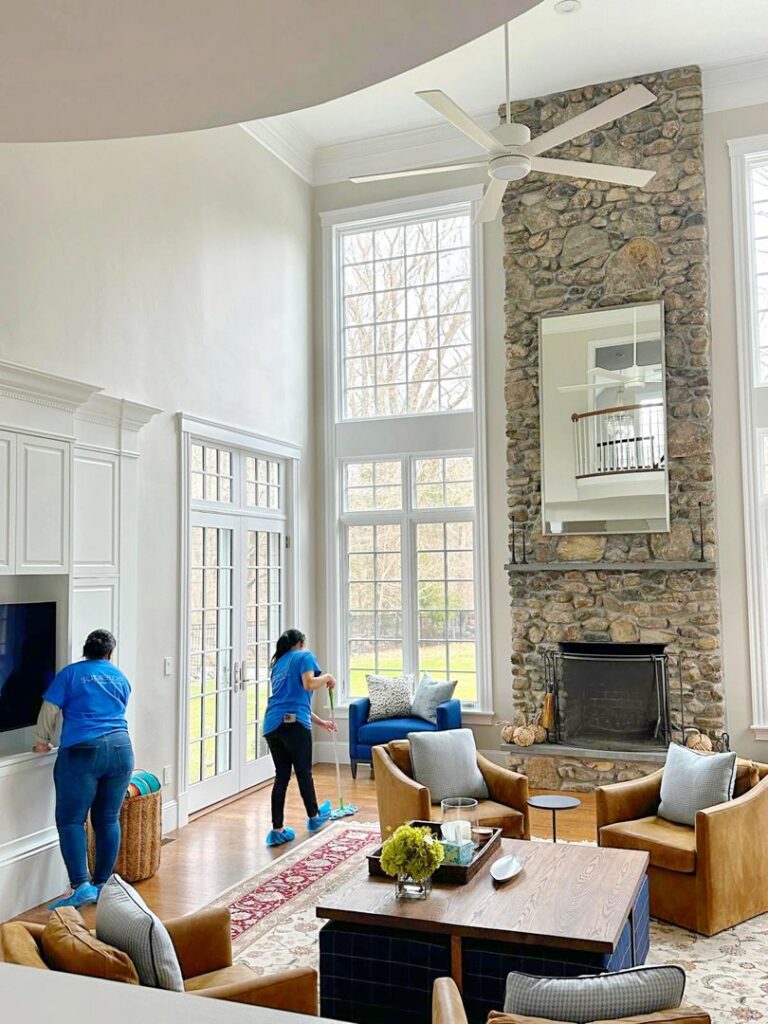 Two professional cleaners from Supreme Home Cleaning, Inc cleaning a spacious living room with high windows in Boston, MA.