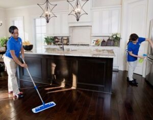 Two professional house cleaners mopping a kitchen floor and wiping a refrigerator at Angel's Services LLC in Alexandria, VA.
