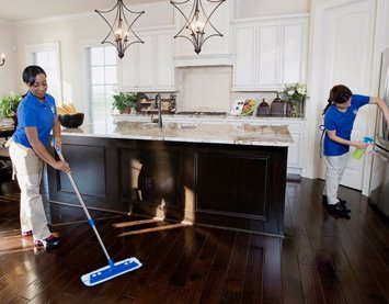 Two professional house cleaners mopping a kitchen floor and wiping a refrigerator at Angel's Services LLC in Alexandria, VA.