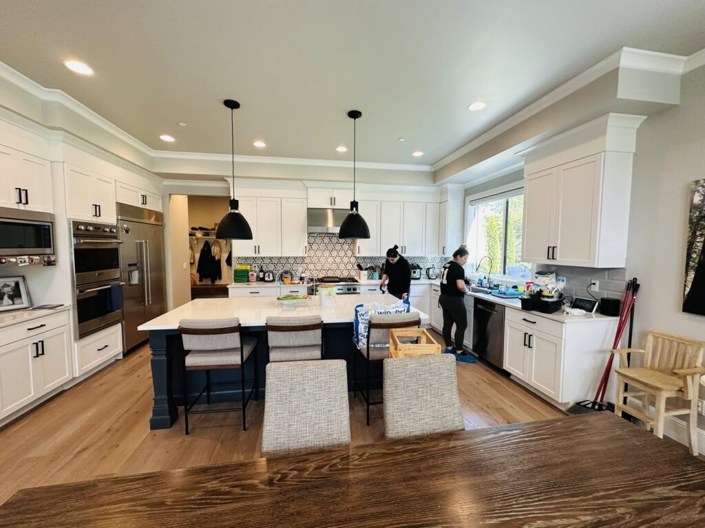 Two professional house cleaners meticulously cleaning a modern kitchen with white cabinets and a large island for Quesada's cleaning services llc in Seattle, WA.