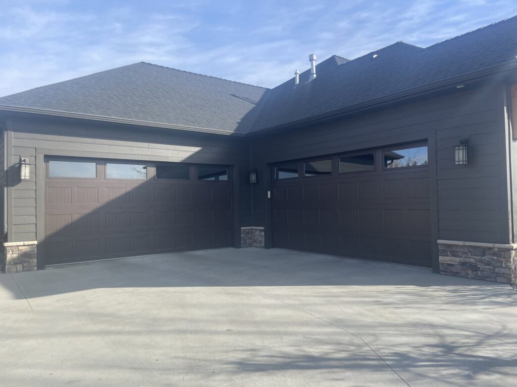 Two dark brown panel garage doors with windows installed on a modern home by Elite Garage Door Service & Repair in Billings, MT.