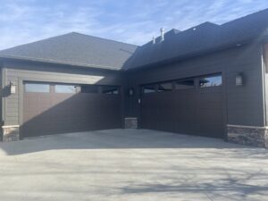 Two dark brown panel garage doors with windows installed on a modern home by Elite Garage Door Service & Repair in Billings, MT.