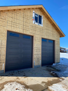 Two dark grey garage doors with windows installed on a new construction home by MBP Garage Doors in Firth, ID