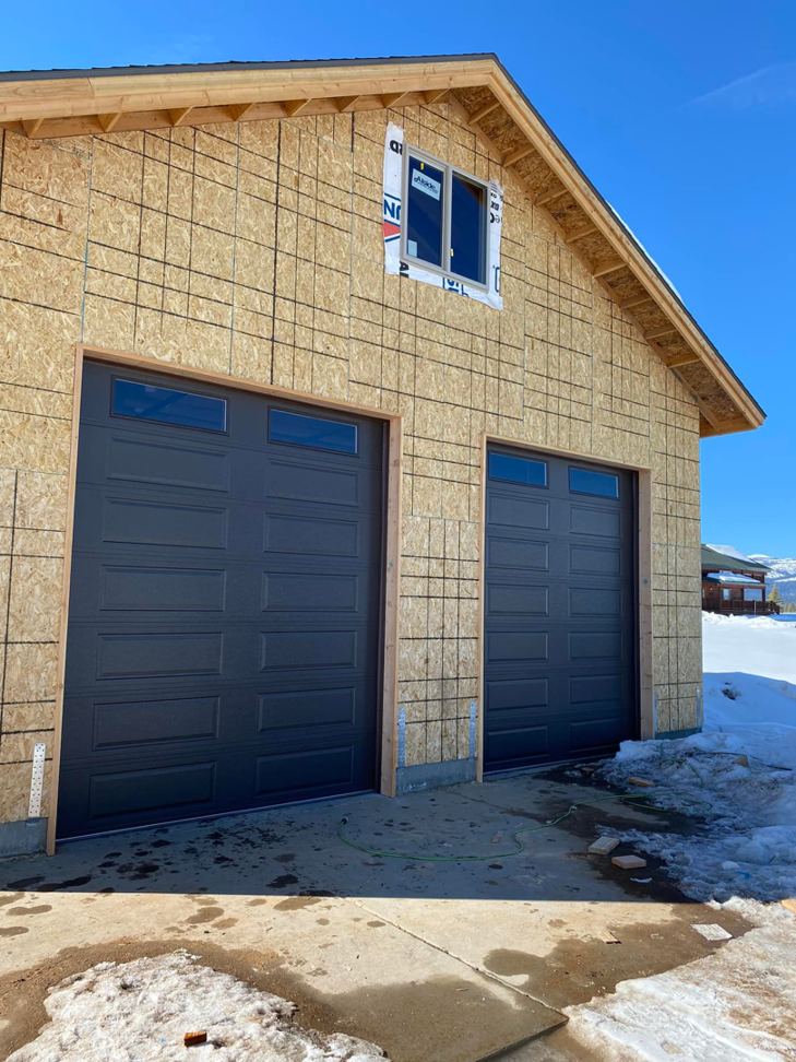 Two dark grey garage doors with windows installed on a new construction home by MBP Garage Doors in Firth, ID