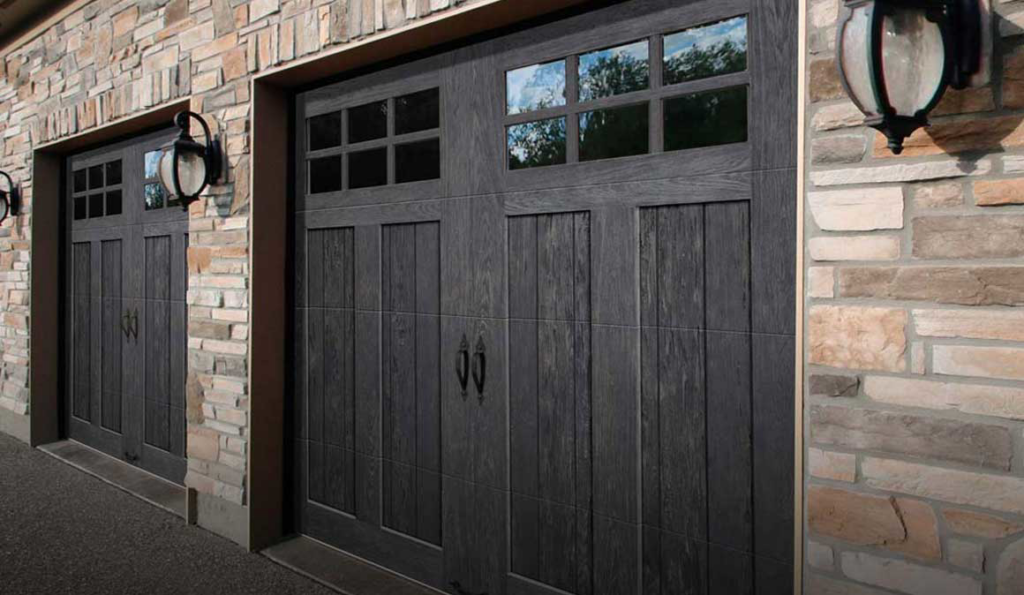 Two dark grey garage doors with decorative windows installed on a stone house by Advance Garage Door, Inc. in Fargo, ND.