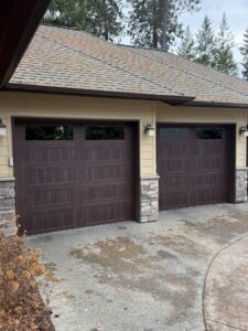 Two dark wood-look garage doors installed on a residential home, showcasing the finished work by North Idaho Garage Door in Coeur d'Alene, ID.