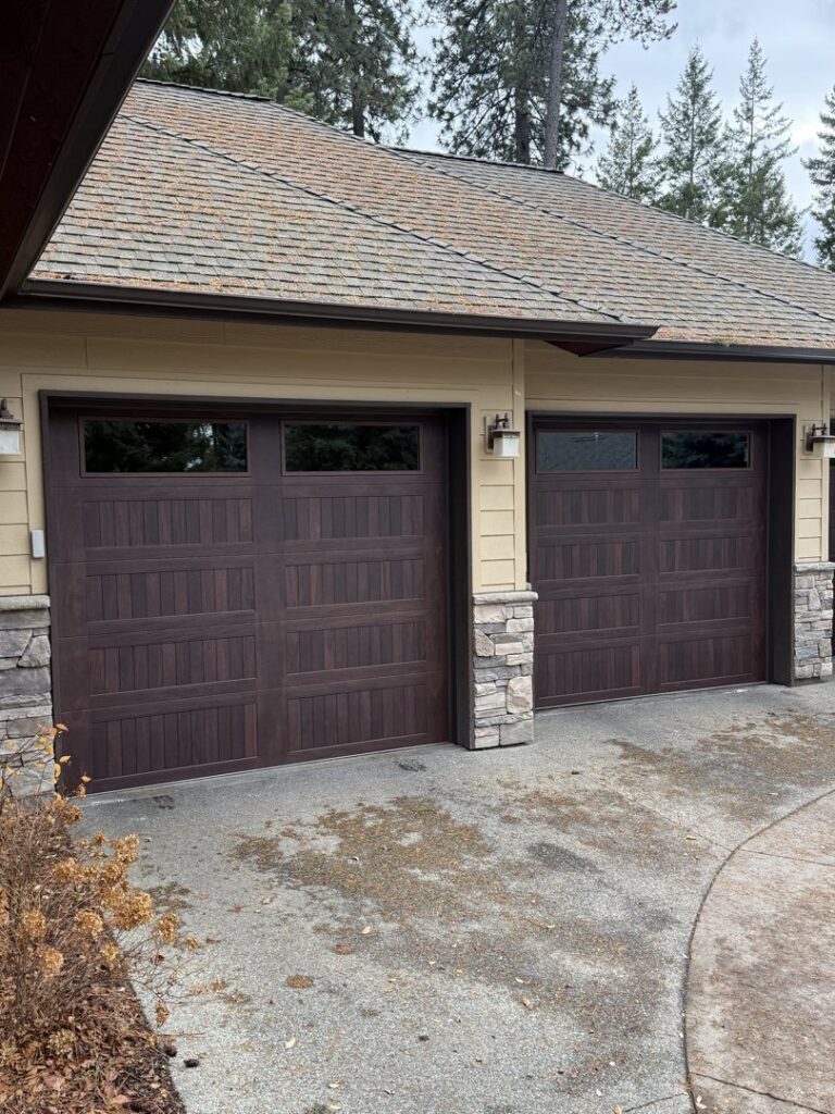 Two dark wood-look garage doors installed on a residential home, showcasing the finished work by North Idaho Garage Door in Coeur d'Alene, ID.
