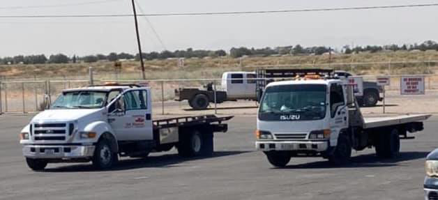 Two white flatbed tow trucks from ROMU Towing parked in a lot in El Paso, TX.