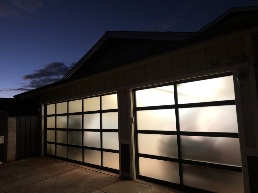 Two modern frosted glass panel garage doors illuminated at dusk, installed by Oahu Garage Doors in Waipahu, HI