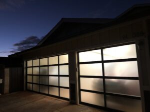Two modern frosted glass panel garage doors illuminated at dusk, installed by Oahu Garage Doors in Waipahu, HI