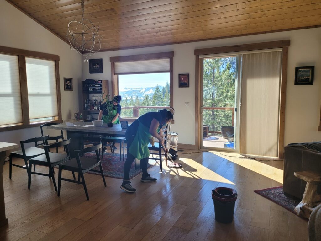 Two professional house cleaners from ECO Friends cleaning service mopping a wooden floor in a spacious home in Carson City, NV.