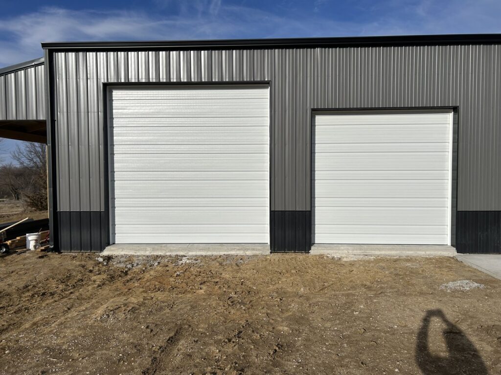 Two white industrial-style garage doors installed on a metal building by Woodwards Overhead Door Co. in Topeka, KS