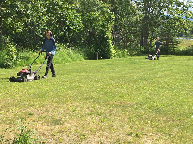 Two Leader Lawns specialists efficiently mowing a large grassy area with push mowers in Anchorage, AK.