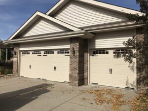 A residential home with two newly installed light beige garage doors by JLM Garage Doors Omaha in Papillion, NE.