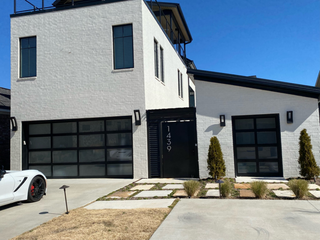 Two modern black glass garage doors on a white brick house, installed by Garage Door Sales & Repair in Conway, AR.