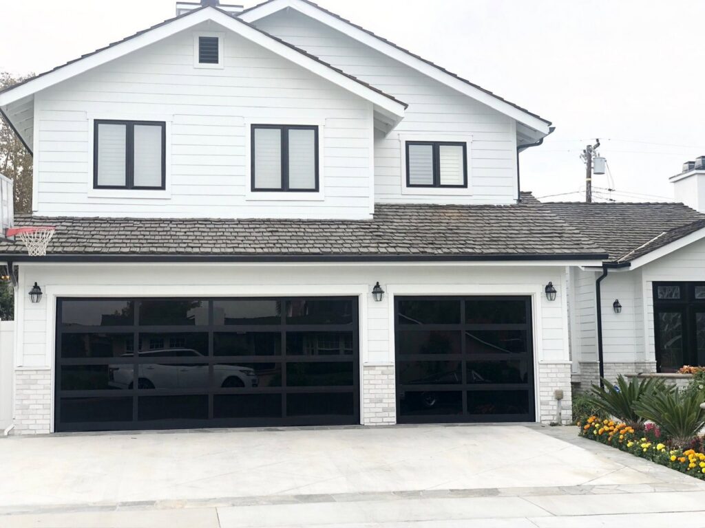 A white residential house featuring two modern black glass garage doors installed by NV Pro Garage Doors in Las Vegas, NV.