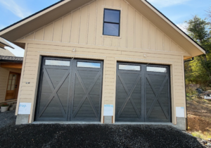 Two modern dark X-brace garage doors with windows installed on a new residential home by Steelhead Doors, Services Available In.