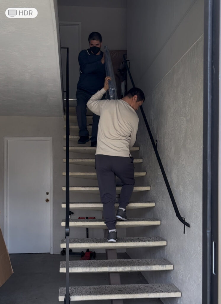 Two movers carrying a long, wrapped item up a staircase for IMoving Professional Moving System Inc. in San Francisco, CA