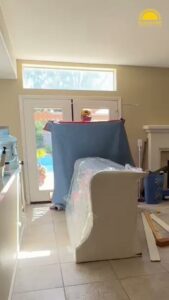 Two professional movers from Sunshine Moving Services LLC carefully carrying a large, wrapped item through a doorway in San Diego, CA.