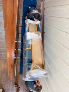 An overhead view of two movers carefully carrying a large, wrapped item down an indoor staircase for All Way Moving in Washington, PA.
