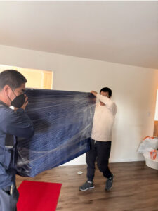 Two movers carrying a wrapped item inside a home for IMoving Professional Moving System Inc. in San Francisco, CA