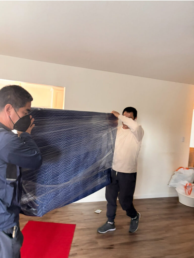 Two movers carrying a wrapped item inside a home for IMoving Professional Moving System Inc. in San Francisco, CA