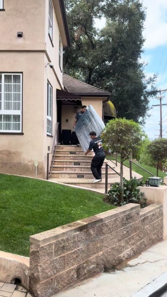Two movers carefully carrying a large, wrapped piece of furniture up outdoor stairs for All Way Moving in Washington, PA.