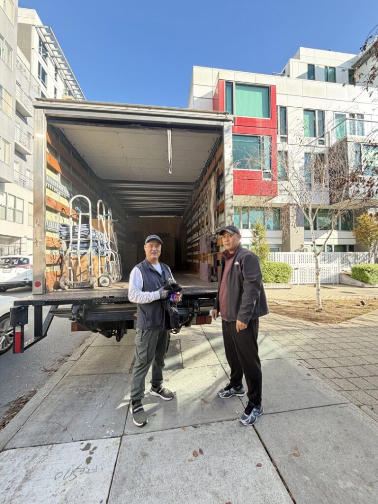 Two movers standing in front of an open IMoving Professional Moving System Inc. truck at a job site in San Francisco, CA