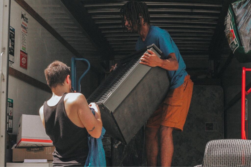 Two professional movers from Ingenuity Moving loading a large piece of furniture into a truck in Kansas City, MO.