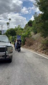 Two movers pushing a large, wrapped item on a dolly up a sloped residential road for All Way Moving in Washington, PA.
