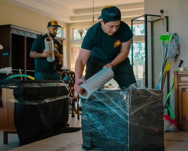 Two professional movers from Sunshine Moving Services LLC carefully wrapping furniture with plastic for protection in San Diego, CA.