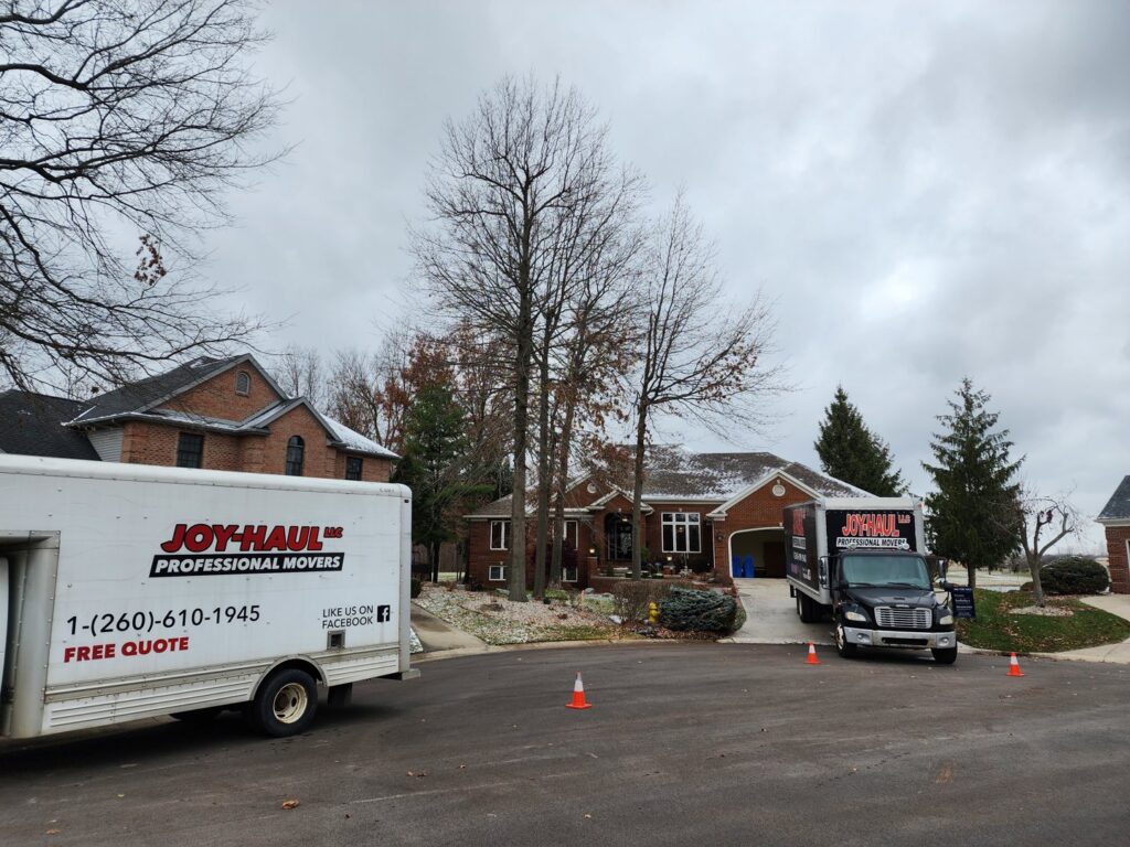 Two Joy Haul Professional Movers trucks parked outside a house, prepared for a moving service in Columbia City, IN.
