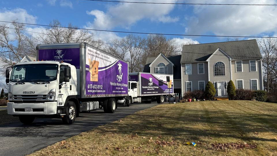 Two Paradise Moving & Storage trucks parked in front of a house in Boston, MA.