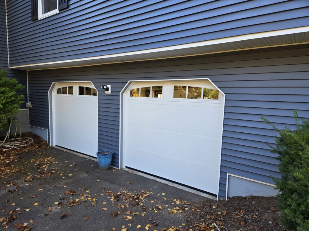 Two newly installed white garage doors on a blue house by Spring King Garage Doors in Middletown, CT
