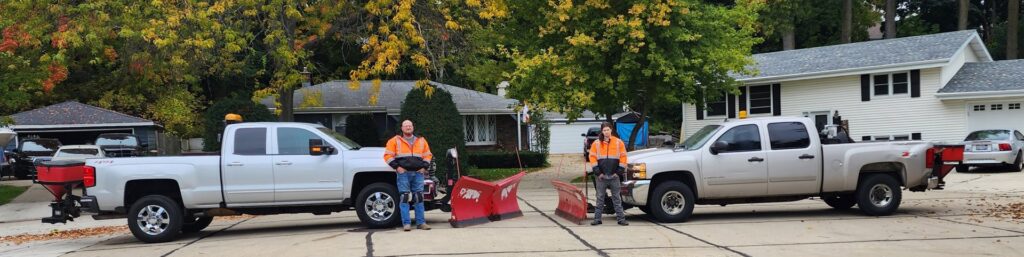 Two snow plow trucks with salt spreaders and crew members, ready for snow removal services from JCO Landscape & SNOW in Racine, WI.