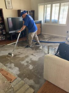 Two technicians from Lotus Restoration Services extracting water from a living room floor during a water damage restoration in Gilbert, AZ.