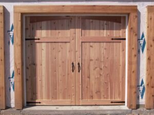 Two unfinished wooden carriage-style garage doors installed on a building under construction by Alberts Custom Door Company in Wichita, KS.