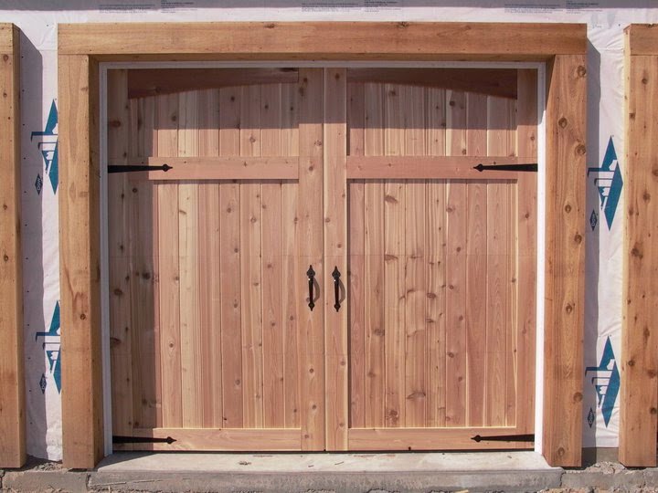 Two unfinished wooden carriage-style garage doors installed on a building under construction by Alberts Custom Door Company in Wichita, KS.