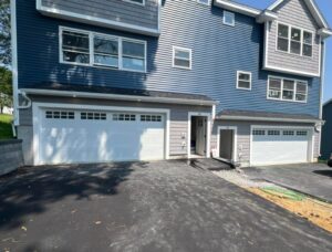 Two white garage doors installed on a blue and gray sided residential building by NDI Garage Door in Plaistow, NH.