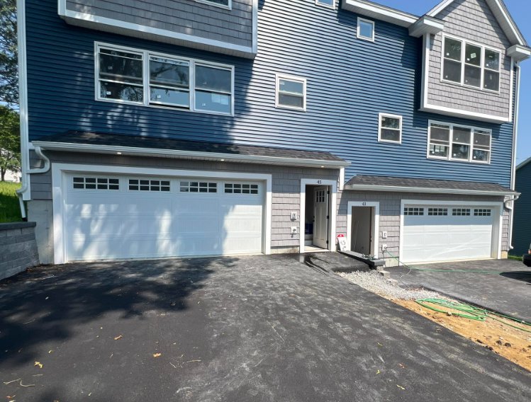Two white garage doors installed on a blue and gray sided residential building by NDI Garage Door in Plaistow, NH.