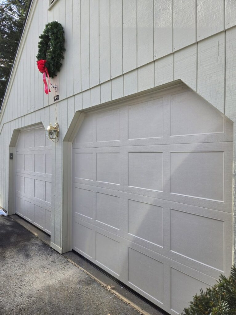 Two newly installed white garage doors on a light-colored house with a Christmas wreath by Spring King Garage Doors in Middletown, CT